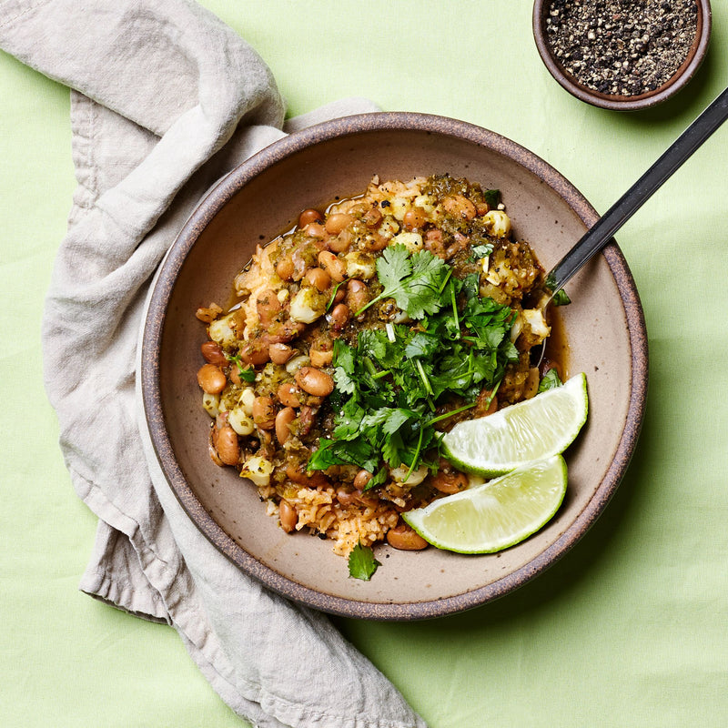 A shallow ceramic bowl filled with a bean soup and topped with cilantro and lime wedges.