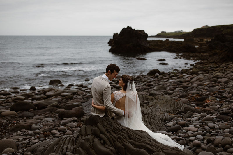 A wedding photo of Eva and James on the coast looking at each other.