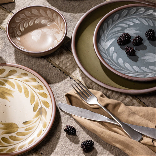 An overhead view of a table with hand painted dinnerware, silverware, napkin, and a coupe glass.