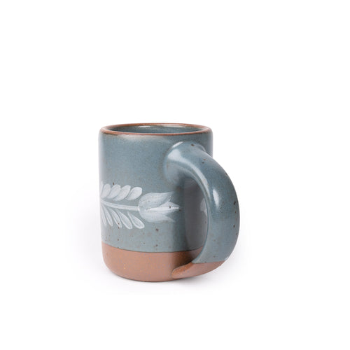 Side profile of Blue-grey ceramic mug with a hand-painted white leaf motif and exposed clay base on a plain white background.