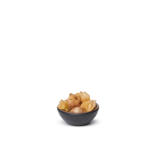 A tiny rounded ceramic bowl in a graphite black color featuring iron speckles and an unglazed rim, filled with food