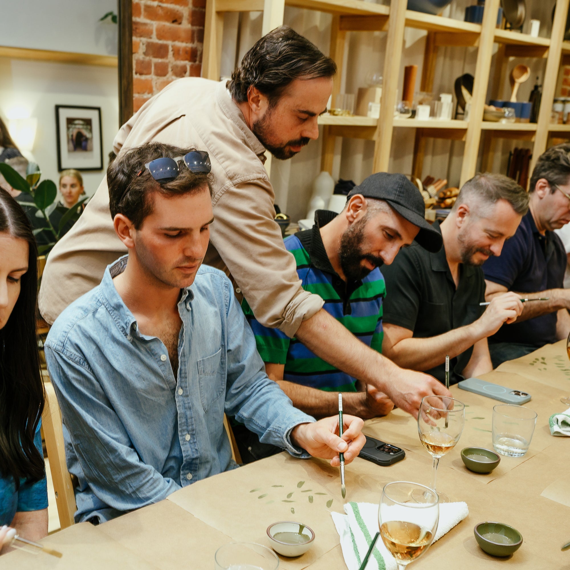 Alex teaching a hand painting workshop in Brooklyn. He is painting on a paper covering a table as students watch and mimic.