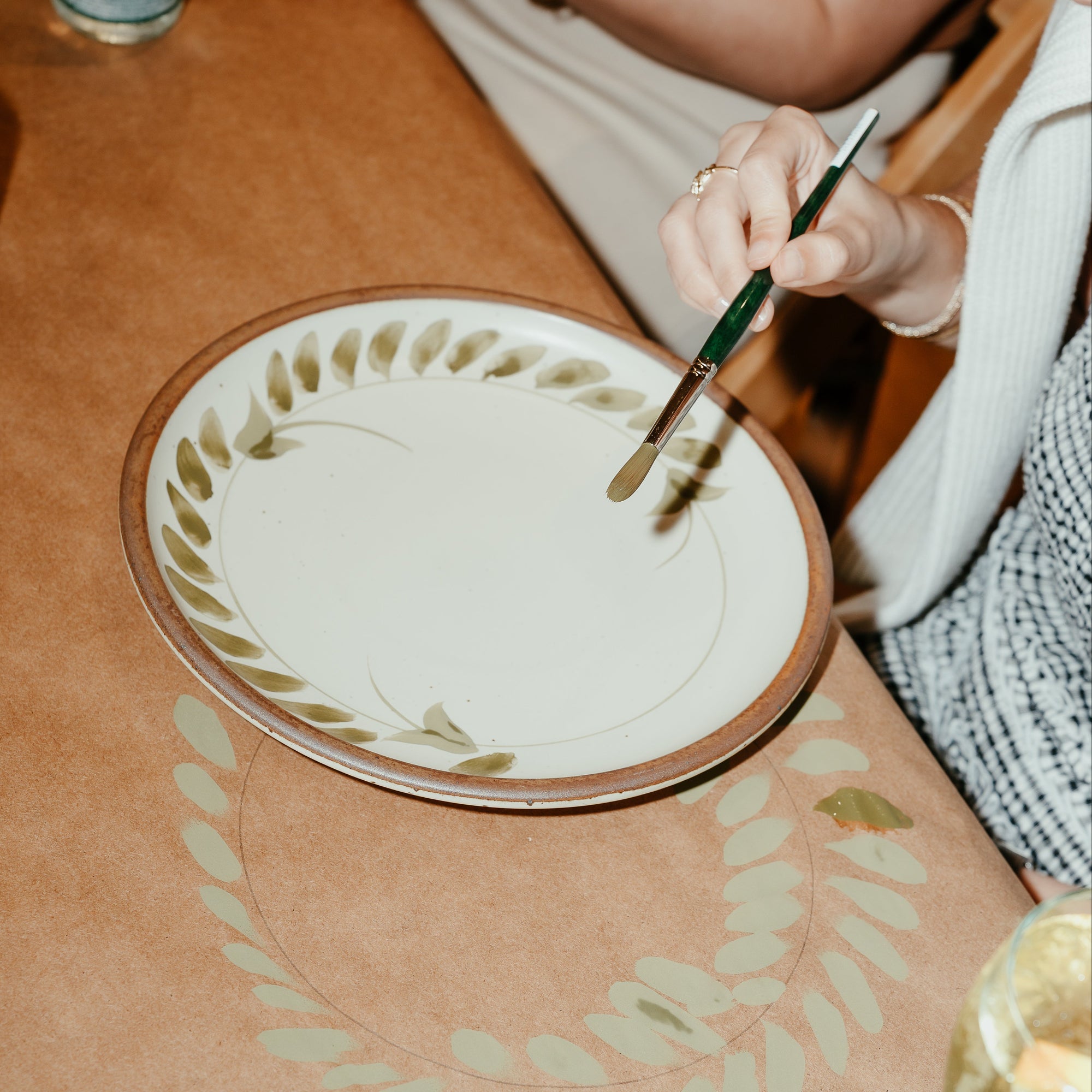 A hand holding a paintbrush painting a plate in a workshop.